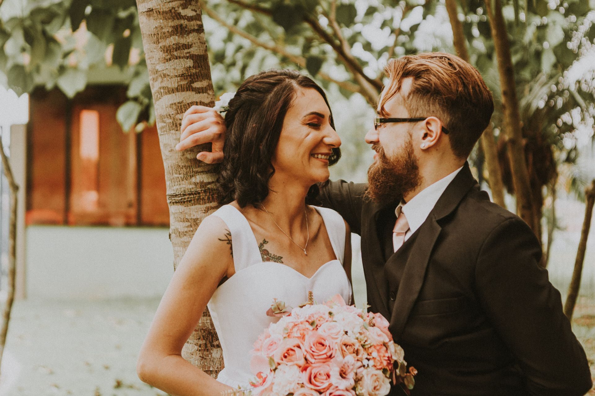 Smiling bride and groom embracing outdoors, the bride holding a bouquet of pink roses
