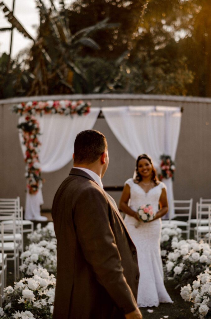 Bride and groom facing each other at a floral outdoor wedding ceremony arch